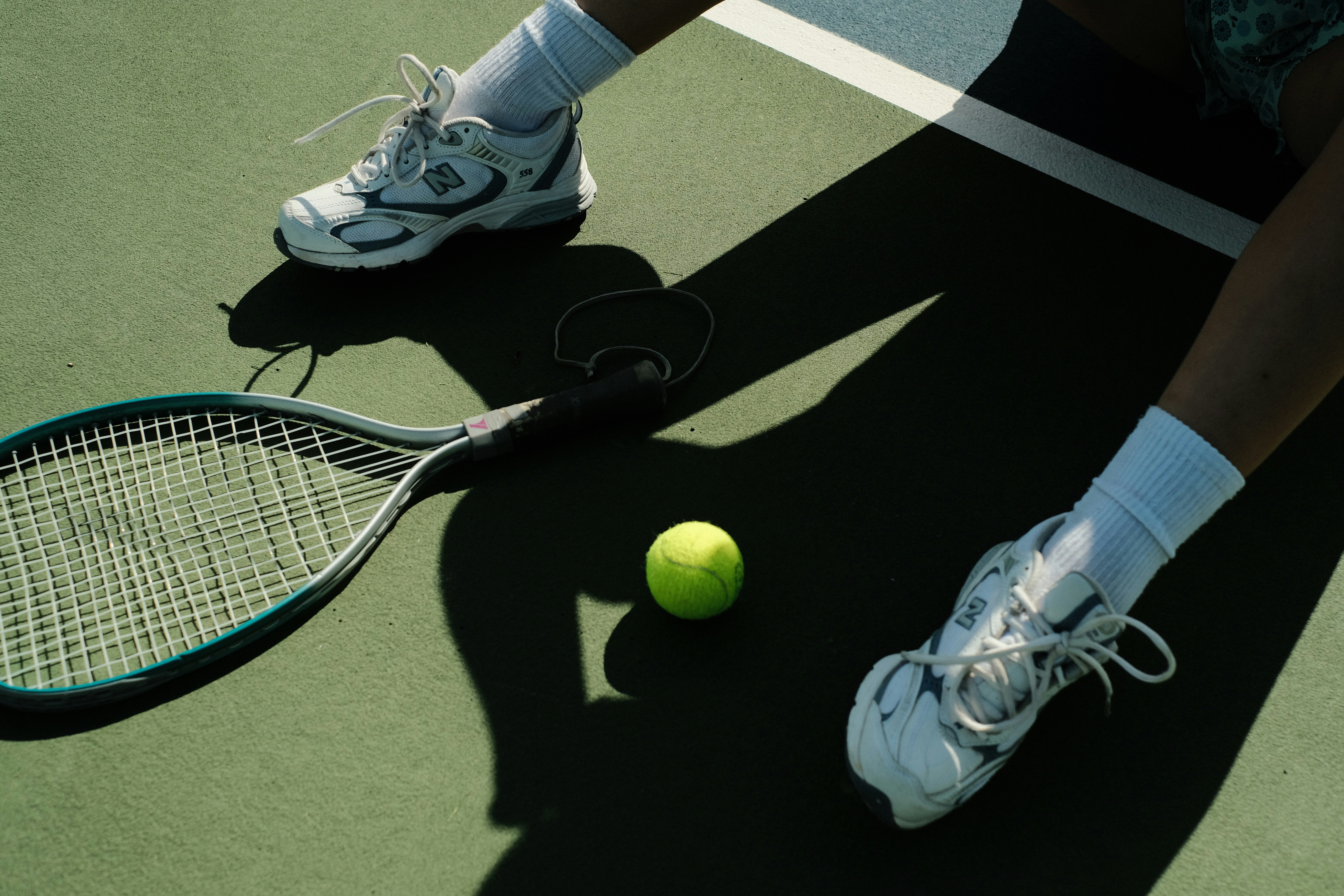 Tennis shoes, racquet, and tennis ball on a green court during a beginner tennis lesson.