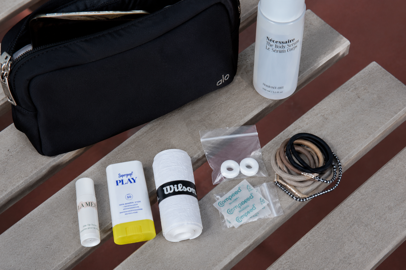 Best tennis accessories for beginners laid out flat including a zip pouch, overgrip, dampener, lip balm, and hair ties — essential items for a beginner tennis bag kit